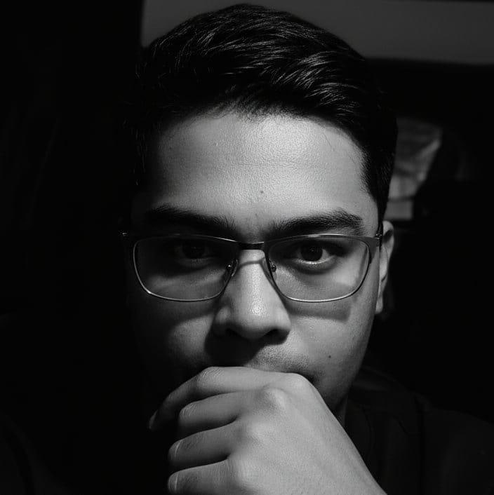 Black-and-white portrait of Raiyan Asaral wearing glasses, hand at his chin.